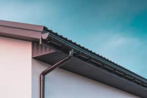 Brown colored plastic gutter on the roof of the building and downspout on the wall