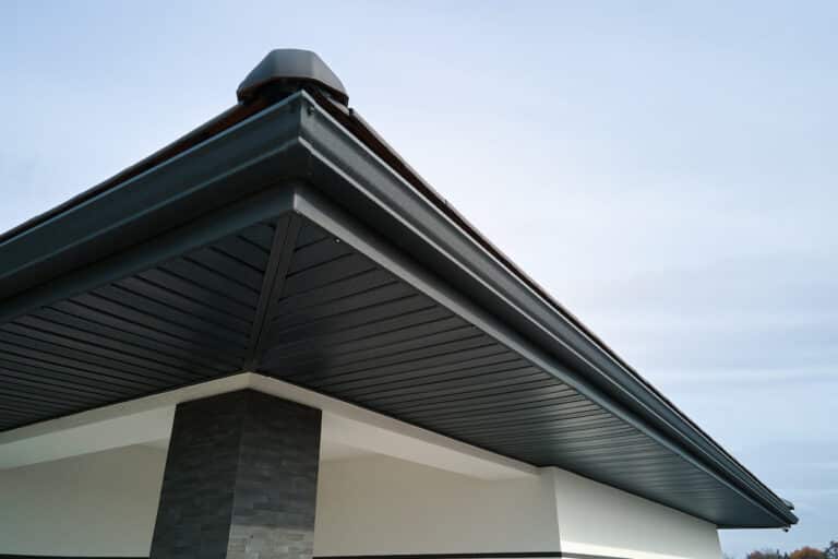 House corner with brown metal planks siding and roof with steel gutter rain system. Roofing, construction, drainage pipes installation